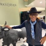 Wilfred Emmanuel Jones MBA smiling to camera, posing with the statue of the cow in store.