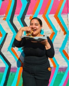 A woman eating a taco outside a bright coloured wall