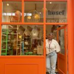 Woman standing in the doorframe of an orange coloured store.