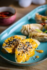 Dumplings covered in a yellow sauce topped with seeds.