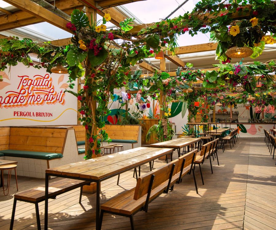 Inside Pergola Brixton rooftop bar, tables and chairs in the sun with floral ceiling decorating