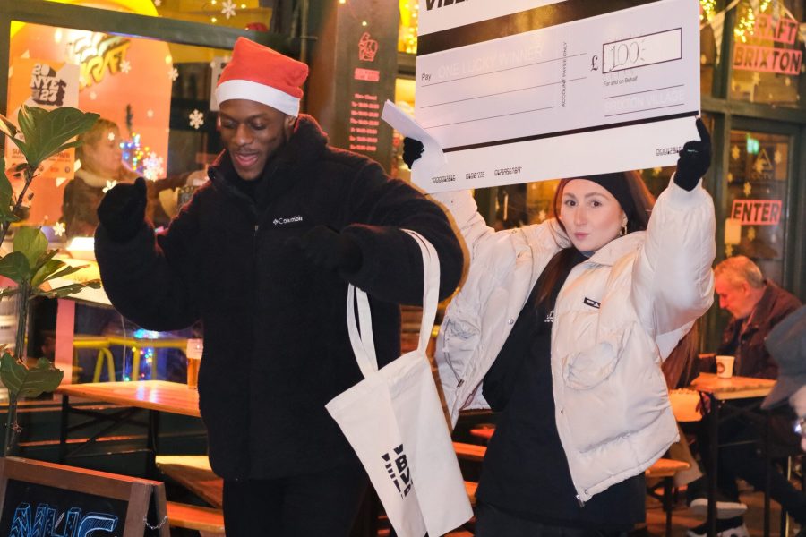 Two Brixton Village promoters in Santa Hats holding a giant cheque.