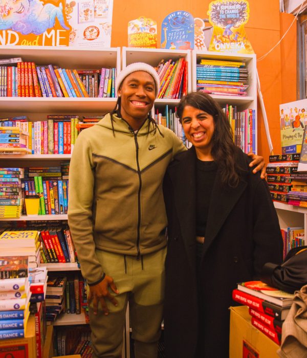 Caster Semenya Signing A Copy of Her Book, smiling to camera inside the book shop.
