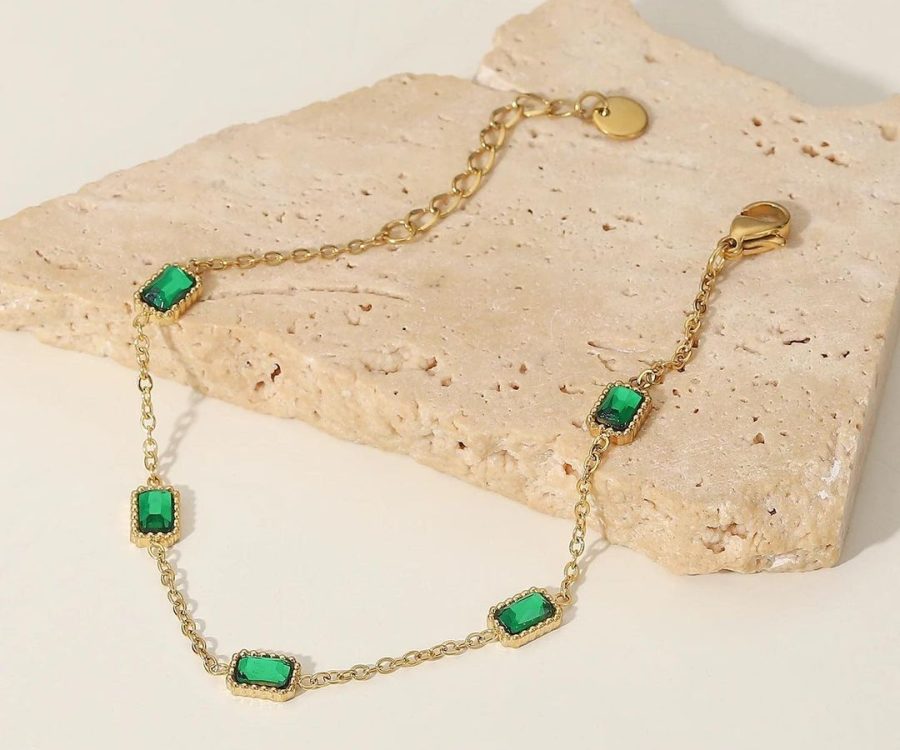 Gold plated and emerald necklace on display on a stone.